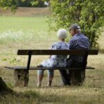Two older adults sitting on a park bench under a tree