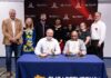 Teo men hold signed agreements with others standing behind them with an engineering school backdrop.