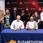 Teo men hold signed agreements with others standing behind them with an engineering school backdrop.