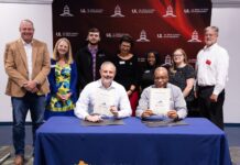 Teo men hold signed agreements with others standing behind them with an engineering school backdrop.