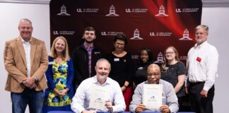 Teo men hold signed agreements with others standing behind them with an engineering school backdrop.