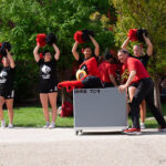 Man pushing the UofL mascot, Louie in a moving cart.