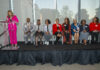 People sit on stage while someone speaks at a podium.