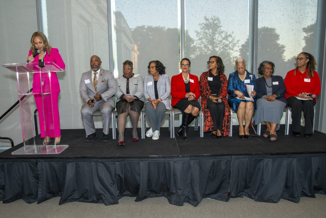 People sit on stage while someone speaks at a podium.