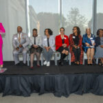 People sit on stage while someone speaks at a podium.