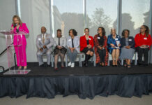 People sit on stage while someone speaks at a podium.