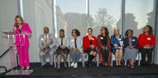 People sit on stage while someone speaks at a podium.