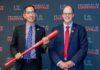 Research!Louisville 2025: Marking 30 years of health sciences research Two men smiling in business suits, one holds a commemorative bat