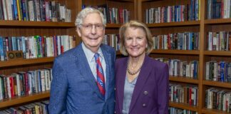 Man and woman stand in a library with shelves of books behind them.
