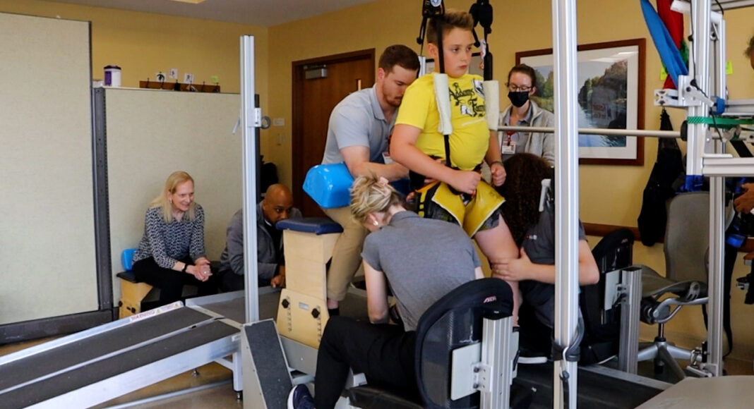 UofL researchers help paralyzed children take steps using external electrical stimulation Child on treadmill assisted by trainers