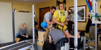 Child on treadmill assisted by trainers