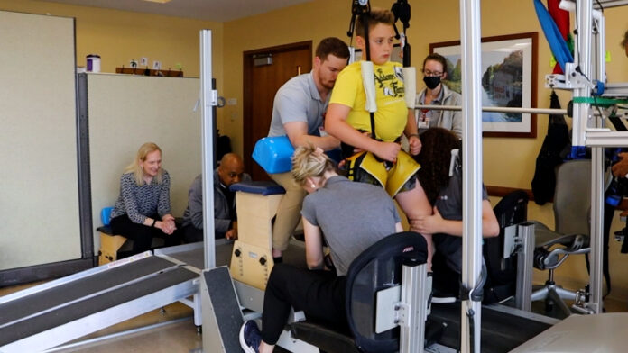 Malcolm on treadmill 2025 Child on treadmill assisted by trainers