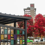 Pergola with colorful panels, red trees and UofL tower in background.