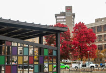 Pergola with colorful panels, red trees and UofL tower in background.