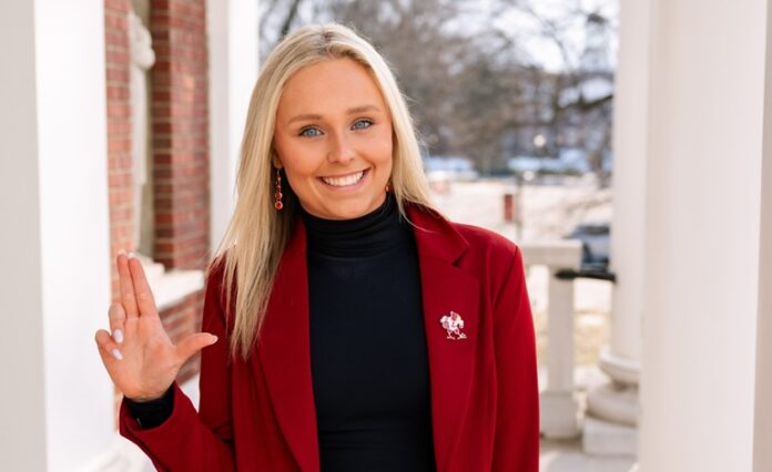 Macy Waddel_cropped Woman in red jacket raises the 'L' sign