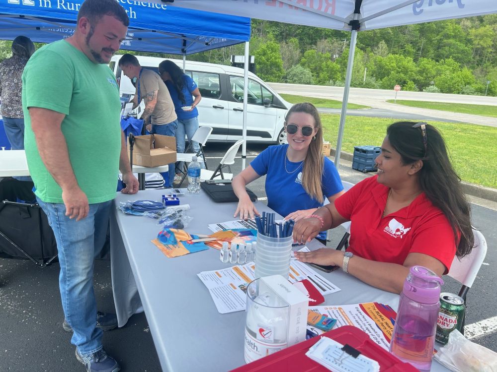 Steph A at Health-Fair-2 rev Women sitting a table talking with a man.