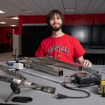 Man, smiling at worktable with assortment of metal and electrical parts
