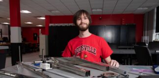 UofL grad embraces the wide world of mechanical engineering Man, smiling at worktable with assortment of metal and electrical parts