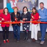 Five people with large scissors cutting a red ribbon