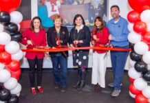 Five people with large scissors cutting a red ribbon