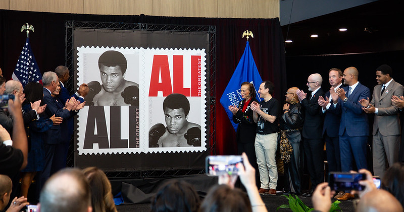 Group clapping as the Muhammad Ali stamp is revealed.