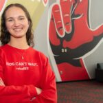 ‘We do good’ : One UofL student’s purpose in loss and raiseRED passion A smiling Carly Lasher crosses her arms in front of a UofL mural.