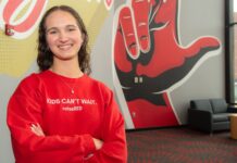 ‘We do good’ : One UofL student’s purpose in loss and raiseRED passion A smiling Carly Lasher crosses her arms in front of a UofL mural.