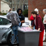 Student carrying clothes on hangers with donor standing next to a bin holding more clothes.