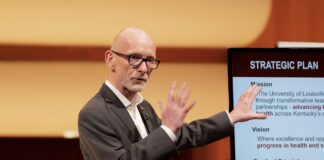 UofL looks to the future in State of University address Man discusses information on slides on a screen behind him.