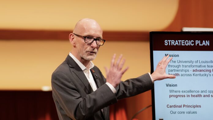 Man discusses information on slides on a screen behind him.