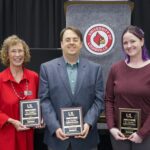 Three individuals holding award plaques