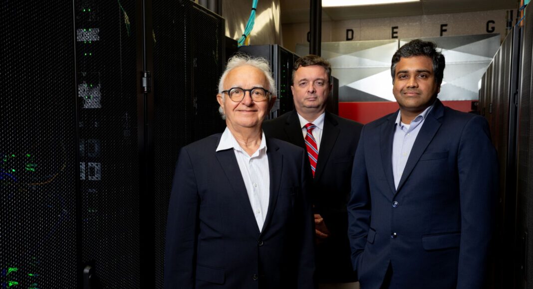 Three men standing in front of banks of computer servers