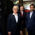 Three men standing in front of banks of computer servers
