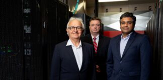 Three men standing in front of banks of computer servers