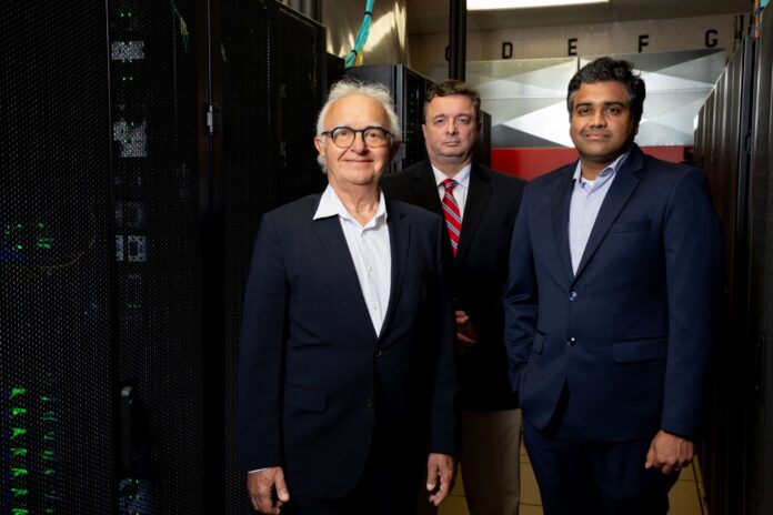 Three men standing in front of banks of computer servers