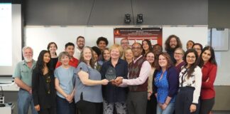 A group stands together with individuals in front holding a glass award.