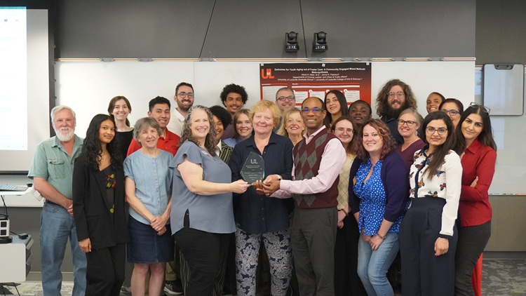 A group stands together with individuals in front holding a glass award.