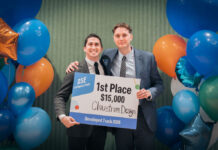 Two male students hold a sign announcing their $15,000 win in a student competition