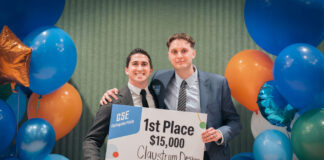 Two male students hold a sign announcing their $15,000 win in a student competition