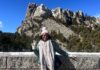 Young woman standing in front of stone wall with Mt. Rushmore monument in background.