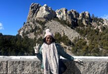 Young woman standing in front of stone wall with Mt. Rushmore monument in background.