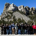 UofL students dressed in warm clothes hold an L's up in front of Mount Rushmore