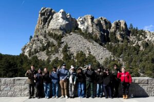 UofL students dressed in warm clothes hold an L's up in front of Mount Rushmore