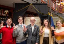 Individuals hold up the L sign with a copy of the Declaration of Independence on display in the background.
