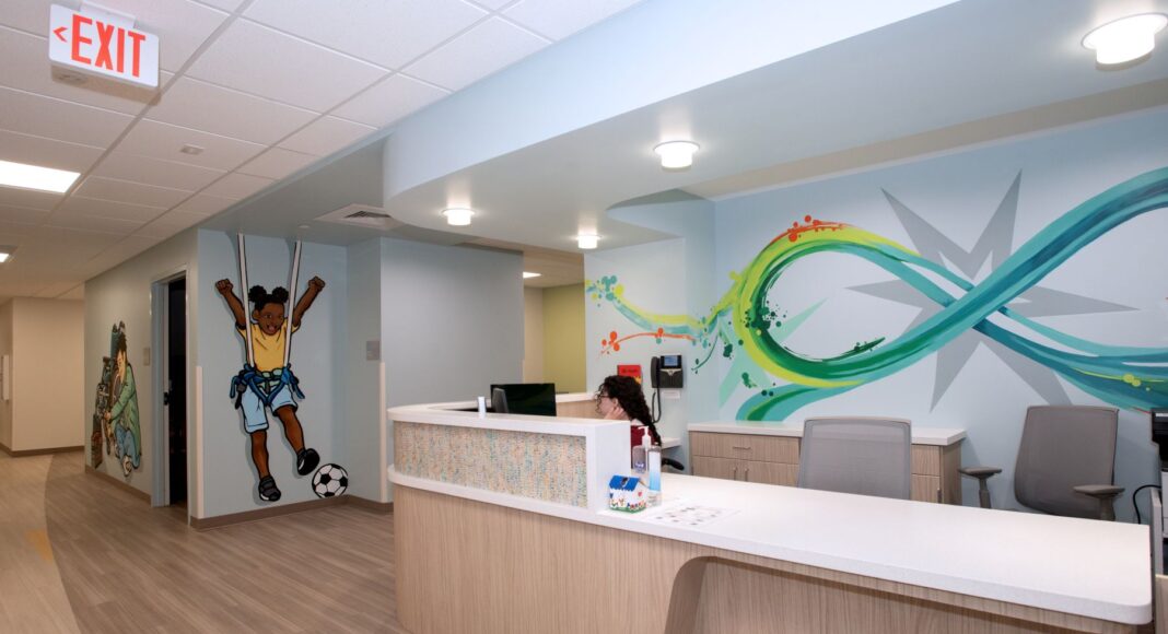 UofL, UofL Health and Kosair for Kids open expanded Pediatric NeuroRecovery Center Reception counter with colorful graphic murals, one includes a young child kicking a soccer ball
