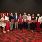 Students smile while holding awards and honors cords at a reception