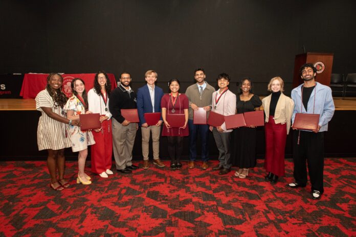 Scholars Students smile while holding awards and honors cords at a reception