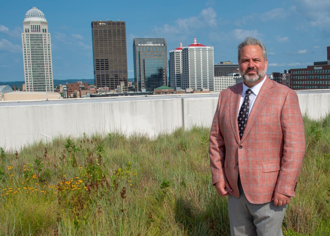 Man on grassy roof with Louisville, Ky. skyline in the background.