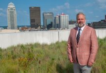Man on grassy roof with Louisville, Ky. skyline in the background.