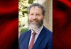 Photo of a man in blue blazer and red tie on a red and black graphic background